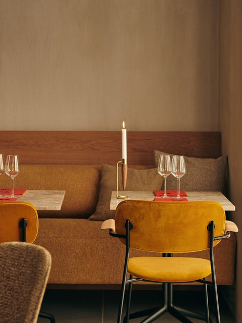 Audo Copenhagen Co Dining Chair, With Arms, Fully Upholstered, yellow, fully upholstered Co Dining Chair with arms in a restaurant, with an Umanoff Candle Holder on a marble table