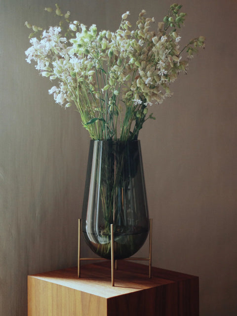 smoked glass vase with brushed brass metal base on a wooden pedestal designed by theresa rand for audo copenhagen