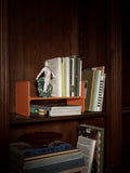 Museum Pedestal by String Furniture in orange turned on its side as a book stand in a wooden bookcase, holding books and a porcelain figurine
