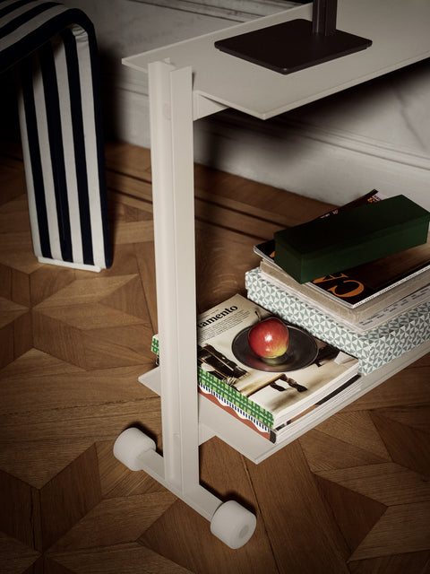 Close-up of the Museum Trolley by String Furniture in white, showing the wheels and lower shelf stacked with magazines
