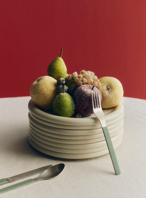 HAY Barro Plates, Ø24, Off-White, glazed terracotta plates, a tall stack topped with sugared fruit and green handled cutlery