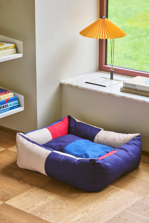 HAY Dog Bed Zip, Medium, Red, Blue, recycled polyester dog bed, on an oak floor by a window with a yellow pleated table lamp