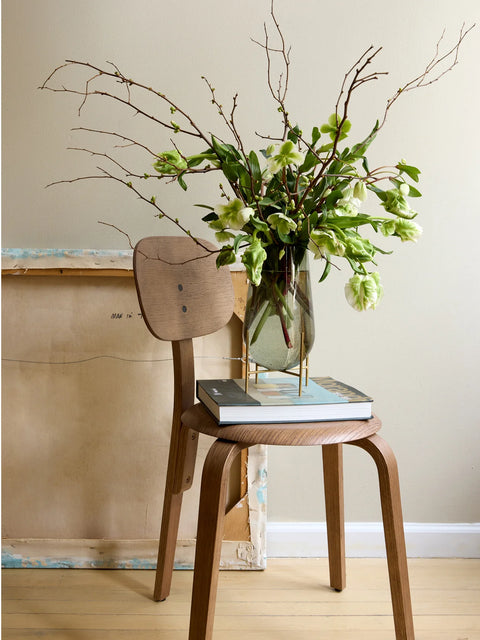 smoked gass with brushed brass metal base on a chair with flowers inside the vase by audo copenhagen