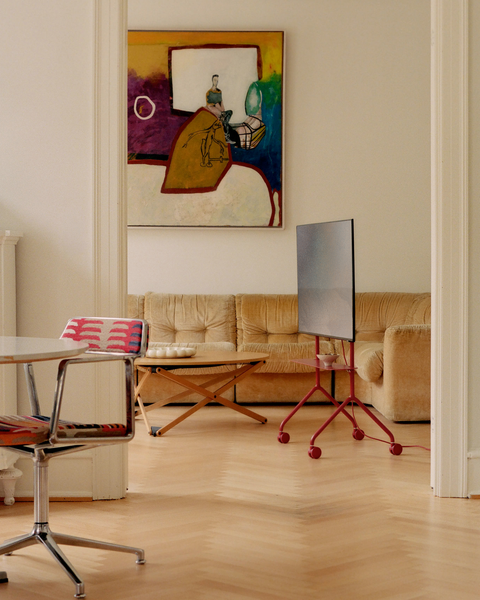 Pedestal Moon Light TV Stand in Burnin' Red, compact steel TV stand on wheels, holding a screen in a living room with a low table and artwork on the wall