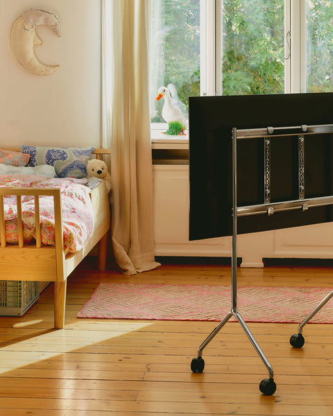 Pedestal Moon Light TV Stand in Chrome, compact steel TV stand on wheels, seen from behind in a child's bedroom beside a cot