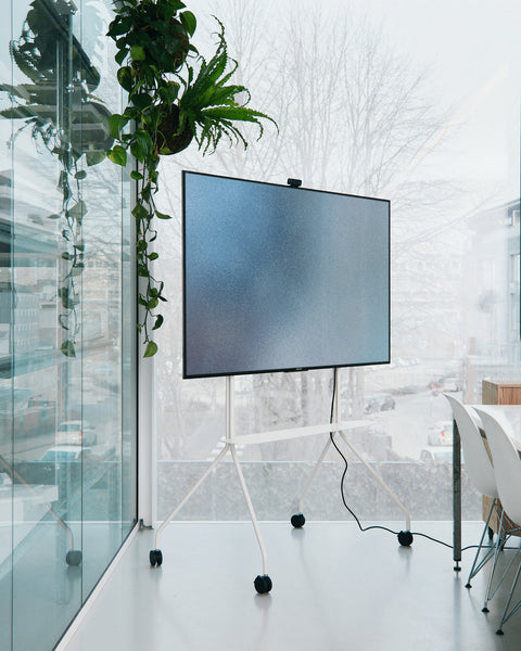 Pedestal Moon PRO TV Stand in Pearl, large mobile TV stand with a shelf, holding a screen in a glazed office with plants