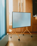 Pedestal Moon Tall TV Stand in Apricot, holding a flat screen beside wooden cabinetry and a blue curtain