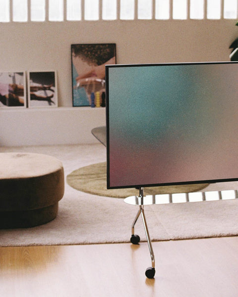 Pedestal Moon TV Stand in Chrome, rolling steel TV stand, holding a screen in a living room with a round coffee table and a pale rug