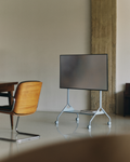 Pedestal Moon Tray Shelf in Powder Blue, steel tray shelf for a TV stand, fitted to a stand in a room beside a wooden chair