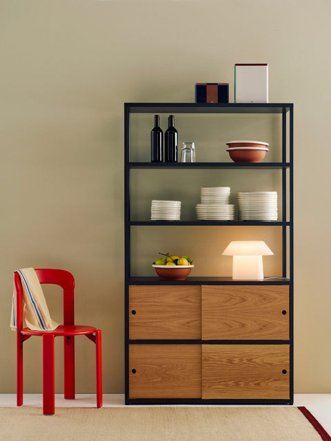 HAY Tin Container, X-Large, Off-White, Burgundy and Green, lidded tinplate storage tin, on black shelving with a red chair and a white lamp