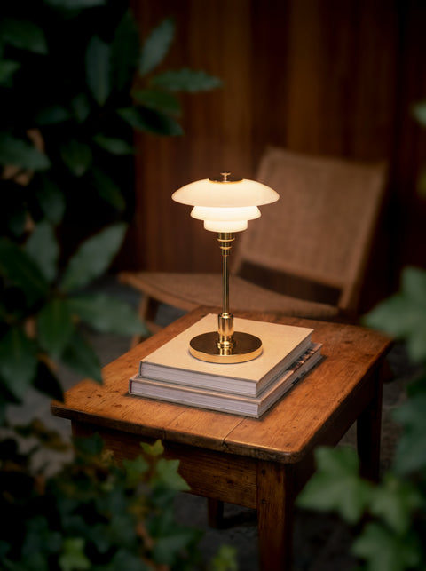 Louis Poulsen PH 1/1 Portable lamp in brass with opal glass shades, lit on a wooden table beside ivy