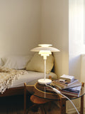 White PH-80 Table Lamp glowing softly on glass side table beside books and beige sofa