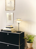 Louis Poulsen PH-80 Table Lamp in chrome displayed on black cabinet beside potted plant and framed art