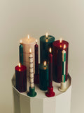 HAY Column Candle, Large, Red Grid Check, stearin pillar candles, a lit group in green, red and cream on a cream ribbed cabinet