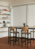 PLAN Barstools in oak and black arranged around a high table in a warm, Scandinavian-inspired room with wall shelving.