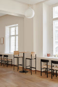 PLAN Barstools in oak and black frame paired with matching high tables in a minimalist light-filled café.