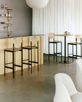 PLAN Barstools in oak and black paired with light wood bar counters and café tables in a cozy dining space.
