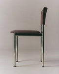 Side profile of Fredericia Plan Chair with dark fabric upholstery and brushed chrome legs