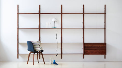 DK3 Royal System Shelving 4 Bay with Drawers in Walnut and Brass, walnut wall shelving with a blue chair, table lamp and a stack of magazines