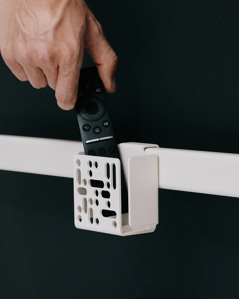 Pedestal Remote Box Mount in Pearl, a hand dropping a remote into the perforated holder on a stand bar