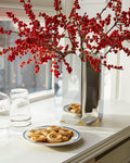 HAY Arcs Vase, Large, Mirror, mirror finish steel vase, with red berry branches on a kitchen counter beside water glasses and cinnamon buns