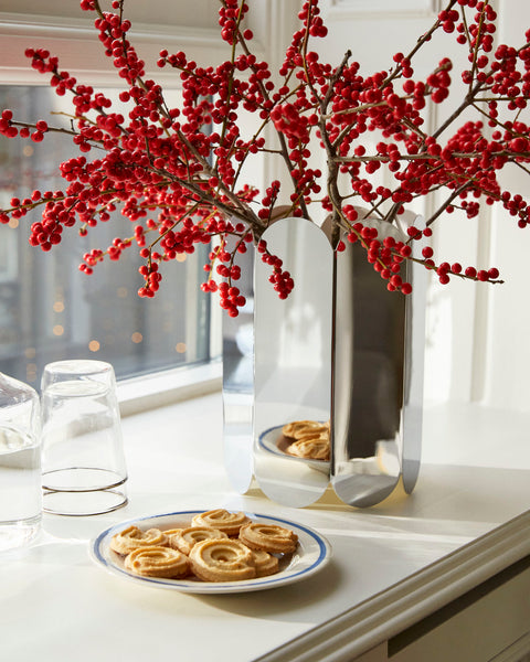 HAY Arcs Vase, Large, Mirror, mirror finish steel vase, with red berry branches on a kitchen counter beside water glasses and cinnamon buns
