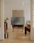 Pedestal Rover TV Stand in Mossy Green, holding a flat screen in a room with a herringbone floor and a pendant lamp