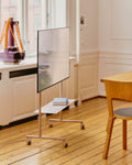 Pedestal Rover TV Stand in Oat, holding a flat screen in a panelled room with a table and chair alongside
