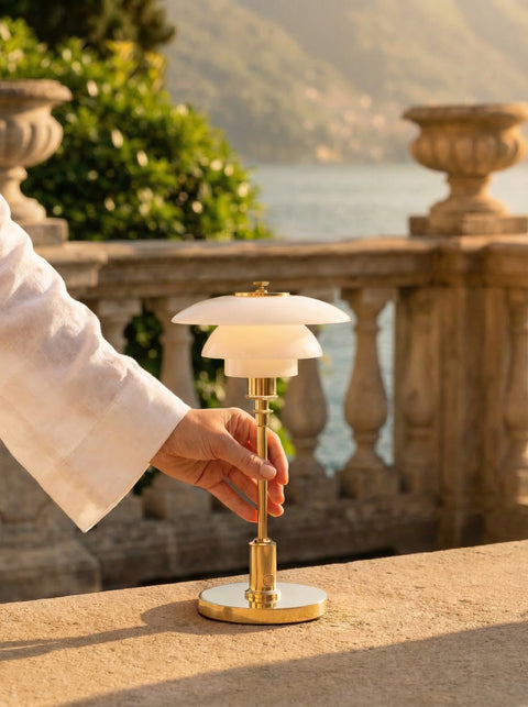Hand reaching for the lit Louis Poulsen PH 1/1 Portable lamp in brass on a sunlit stone terrace