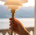Close-up of the Louis Poulsen PH 1/1 Portable lamp in brass with opal glass shades held by a stone balustrade