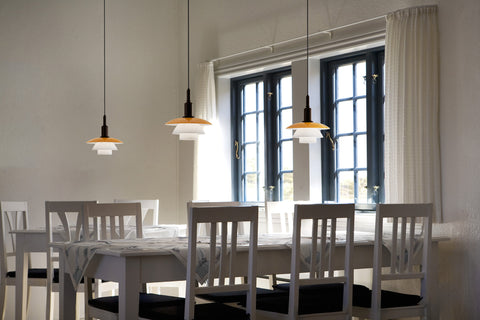 Three Louis Poulsen PH 3/3 Pendant Centenary Edition lamps lit in a row above a long dining table with white chairs
