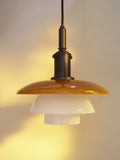 Close-up of the lit Louis Poulsen PH 3/3 Pendant Centenary Edition, the amber shade casting a warm glow across the wall