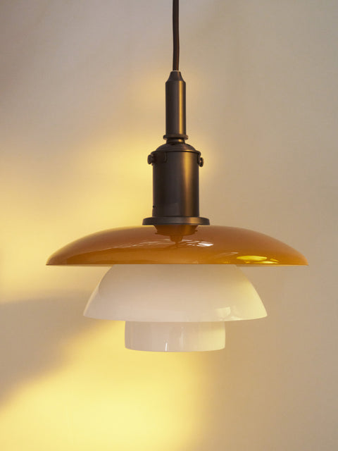 Close-up of the lit Louis Poulsen PH 3/3 Pendant Centenary Edition, the amber shade casting a warm glow across the wall