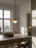 Louis Poulsen PH 3/3 Pendant Centenary Edition lit above a dark dining table holding a carved wooden bowl, in a white panelled room