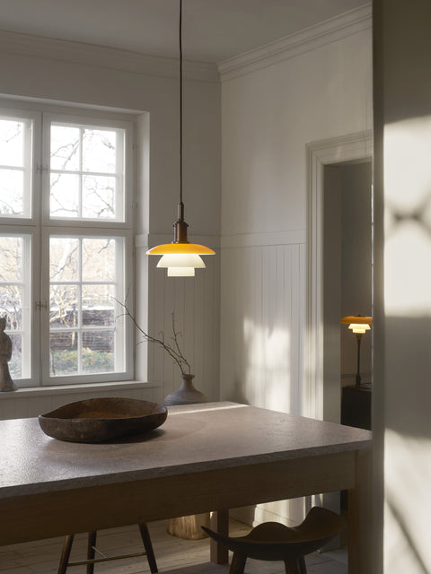Louis Poulsen PH 3/3 Pendant Centenary Edition lit above a dark dining table holding a carved wooden bowl, in a white panelled room