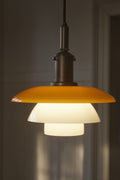 Louis Poulsen PH 3/3 Pendant Centenary Edition lit in a darkened interior, showing the amber upper shade and aged brass shade holder