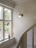 Louis Poulsen PH 2/2 Wall Lamp Centenary Edition lit on a stair landing wall beside a window overlooking a garden