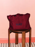 HAY Shopper Bag, Burgundy, cotton tote bag, burgundy shopper on a dark wood stool by a pink wall above chequered tiles
