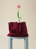 HAY Shopper Bag, Burgundy, cotton tote bag, burgundy shopper on a pale blue stool with a pink tulip stem rising from it