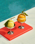 HAY Italian Ice Cup, Stainless Steel, stainless steel ice cream cup, two cups holding an orange and a lemon on a red board by turquoise water