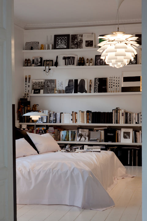 White Louis Poulsen PH Artichoke pendant lighting a serene bedroom with white bedding and wall shelves filled with books and art