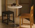 Frama Table 57 in White HDPE, white topped table holding a carafe and two glasses, with a dark stool and a wooden chair beside it