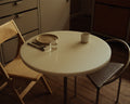 Frama Table 57 in White HDPE, round white top set with a plate, cutlery and a cup on slim dark legs, folding chair and metal chair beside it