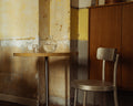 Frama Table 57 in Yellow Limestone, stone topped table with a glass carafe against a patinated wall, a metal chair standing to the right