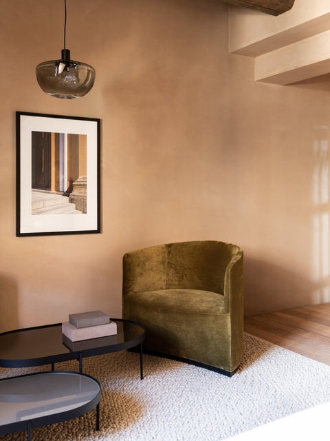 Audo Copenhagen Tearoom Chairs and Sofas, green velvet Tearoom Lounge Chair rests on a textured white rug by black oval coffee tables in a room with beige walls