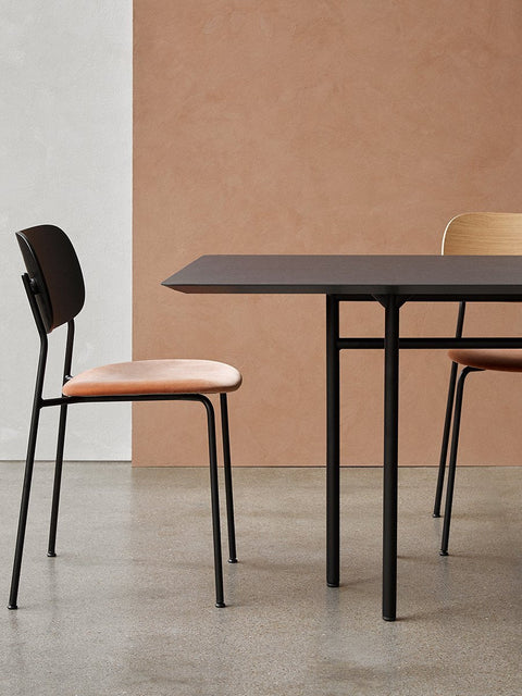 Audo Copenhagen Co Dining Chair, Non-Upholstered, Co Dining Chair with a black frame and coral upholstered seat at a black dining table, against a white and terracotta wall