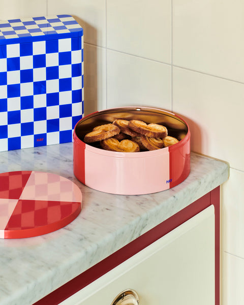 HAY Tin Container, Large, Blue and Off-White, lidded tinplate storage tin, on a marble counter beside a round pink tin filled with pastries
