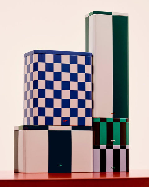 HAY Tin Container, Large, Blue and Off-White, lidded tinplate storage tin, stacked with green and lavender tins on a red plinth, pink backdrop