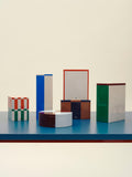 HAY Tin Container, Large, Off-White and Red, lidded tinplate storage tin, lined up with six other tins on a blue shelf against a cream backdrop