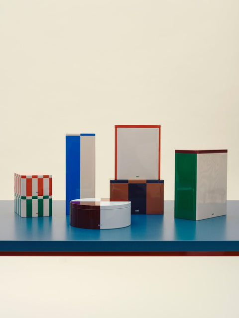 HAY Tin Container, Large, Off-White and Red, lidded tinplate storage tin, lined up with six other tins on a blue shelf against a cream backdrop